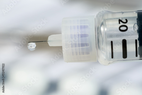 Macro view of drop of insulin hanging on pen's needle. Inside the drop of the hormone are reflected other diabetes medicines and a notebook for blood tests results