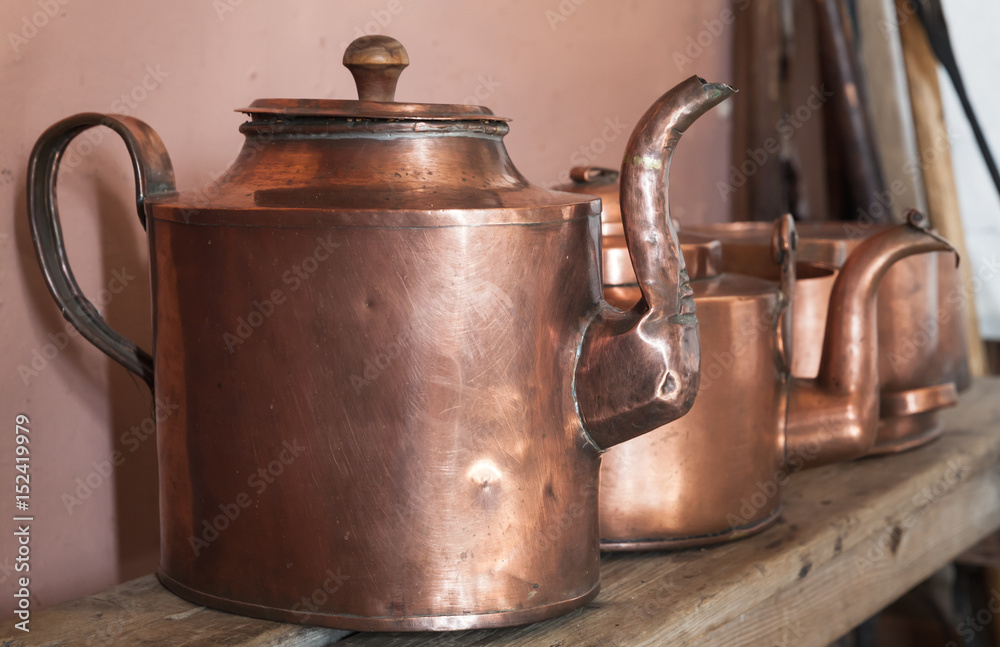 Vintage copper teapots stand on shelf