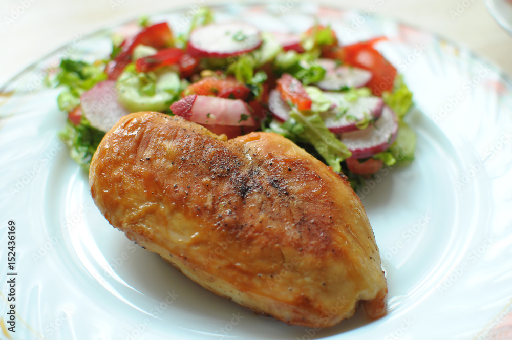 Baked chicken breast with vegetable salad on a white plate