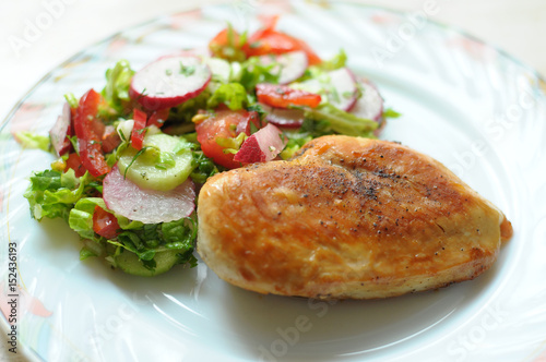 Baked chicken breast with vegetable salad on a white plate