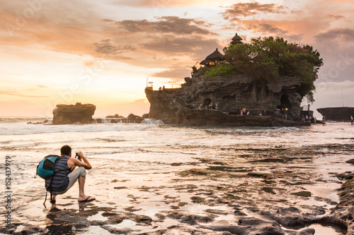 Foto Traveler Man taking photo of beautiful tanah lot landscape during sunset, Ancient hinduism temple Tanah lot on the rock against sunset sky