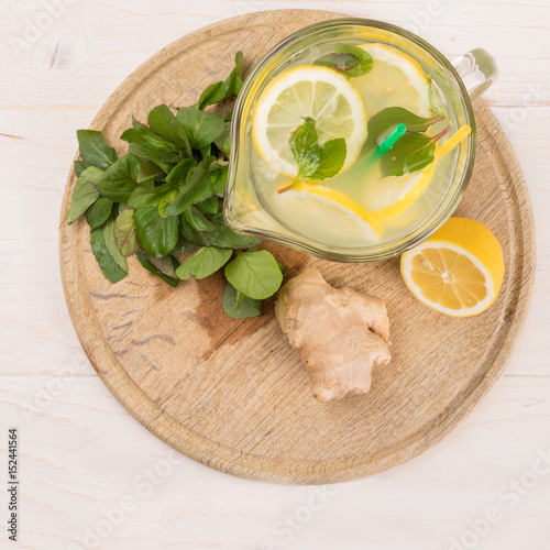 A glass decanter with a summer refreshing lemonade made of lemons and ginger with mint added on a white wooden background. Detox water. Ingredients. Cleaning the body of toxins, vitamins