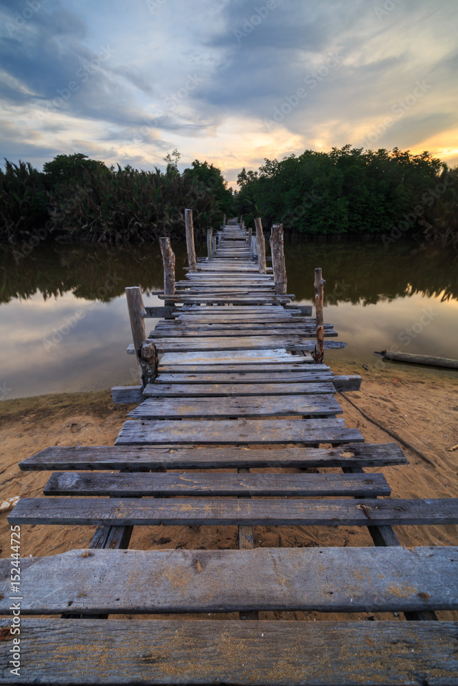 Obraz premium The old wooden bridge over a river at Kg. Pulau Kerengga, Marang Malaysia with sunset scenery