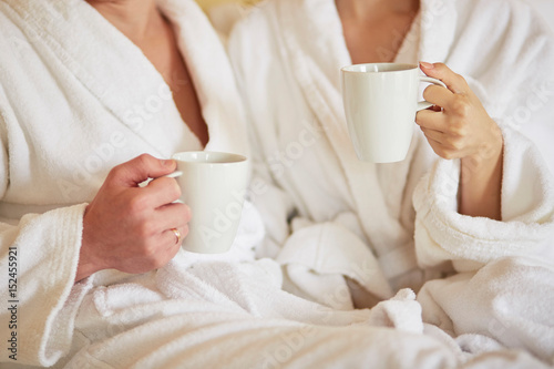 Canvas Print Couple in white bathrobes in bed, drinking coffee