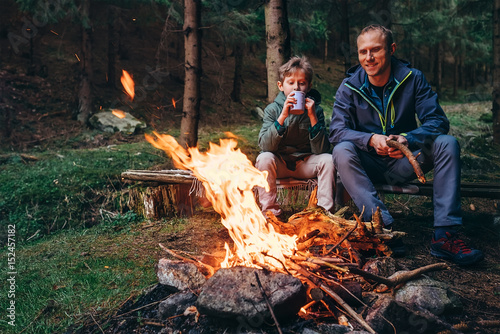 Father and son warm near campfire on forest picnic