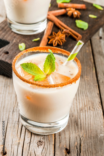 Traditional Indian drink is iced tea or chai masala, with ice cubes from chai, milk and mint leaves. With striped straws, on a wooden board. On an old rustic wooden table. Copy space