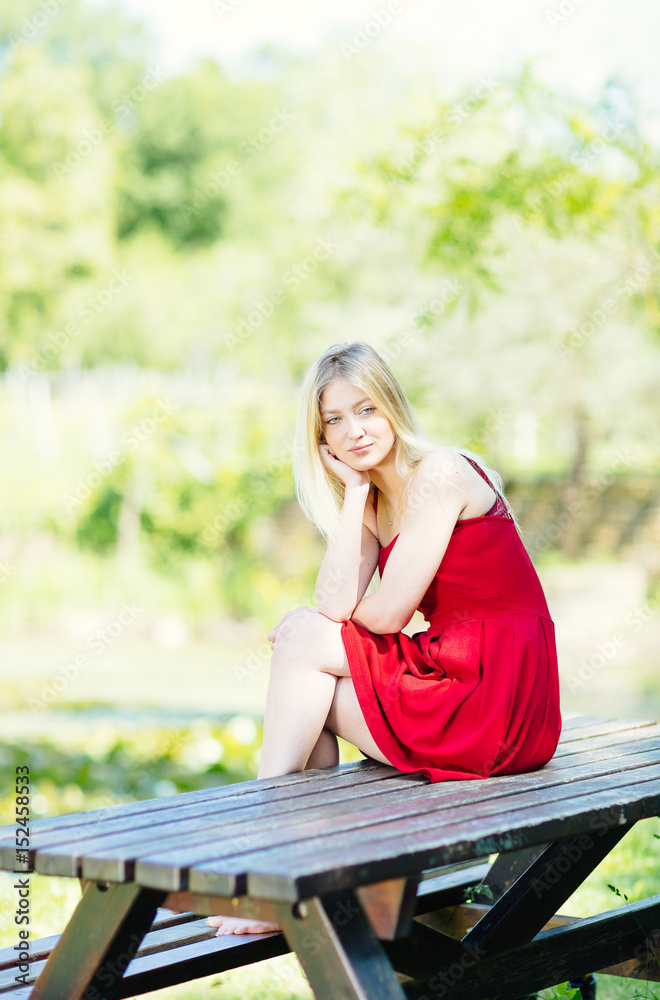 Young blonde woman sitting on the table in the park. Teenager fashion lifestyle. Young blonde woman sitting on the table in the park. Teenager fashion lifestyle.