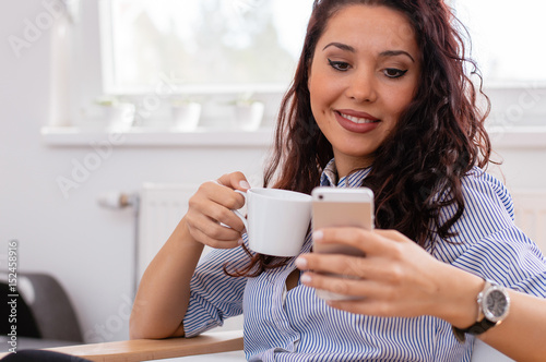 Young woman at home drinking coffee and using mobile phone