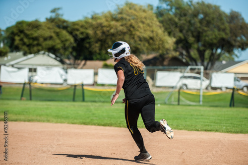 Black uniform softball running around to second base. 