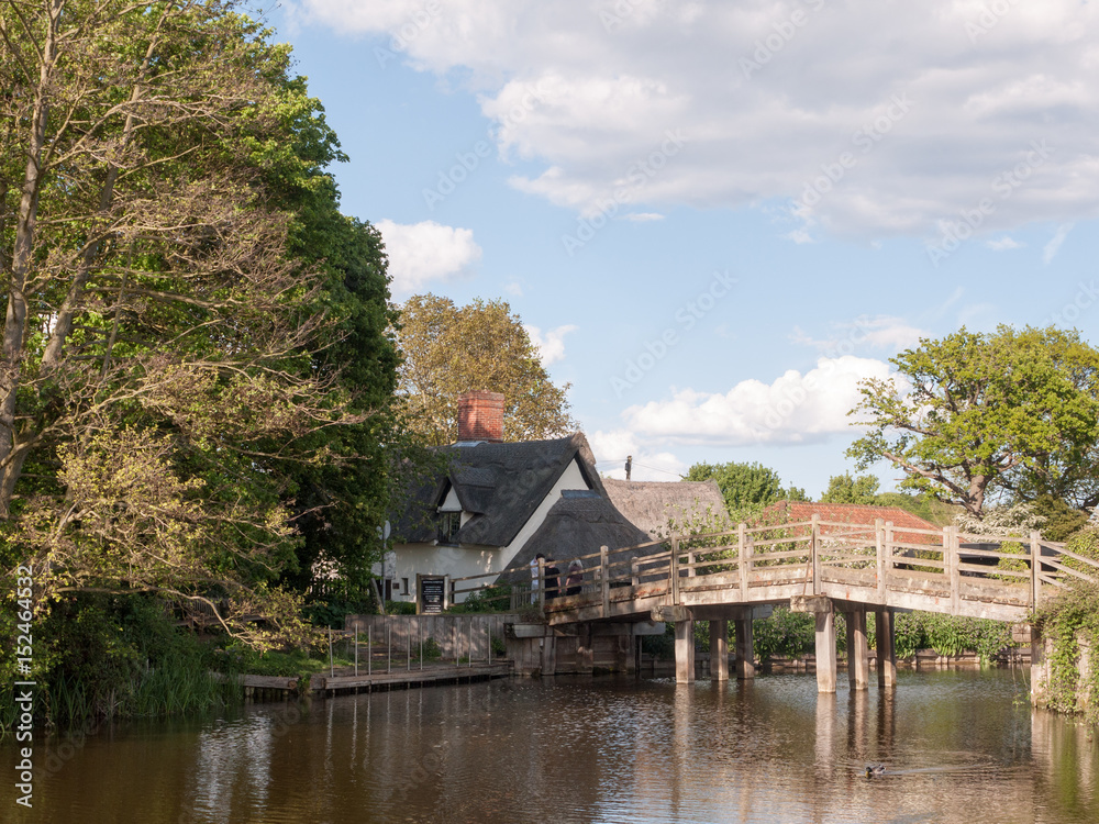 the bridge at flatford mill leading to a cottage in the heartland of constable country essex and suffolk near Dedham with people on the bridge viewing on a sunny relaxing afternoon the bridge at flatford mill leading to a cottage in the heartland of constable country essex and suffolk near Dedham with people on the bridge viewing on a sunny relaxing afternoon