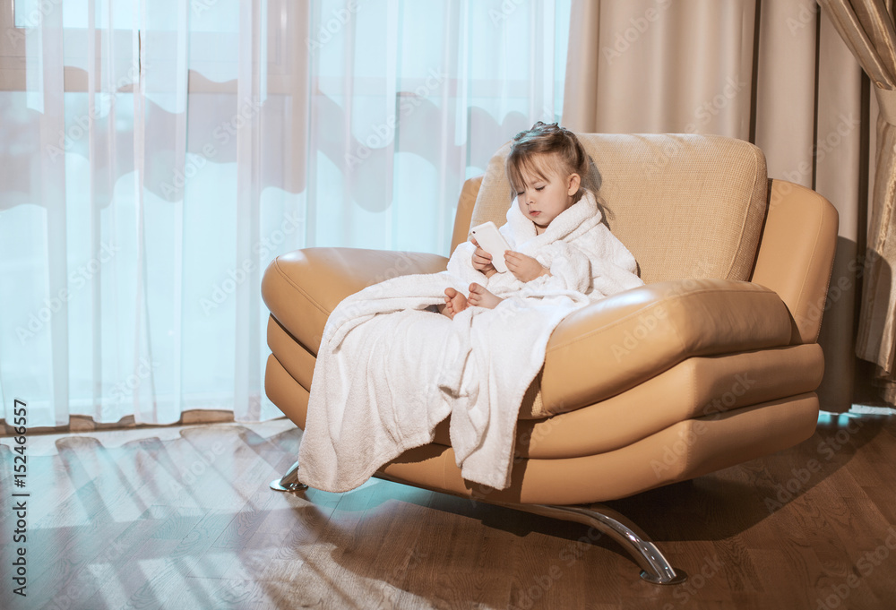 Little girl in white robe plays with mobile phone