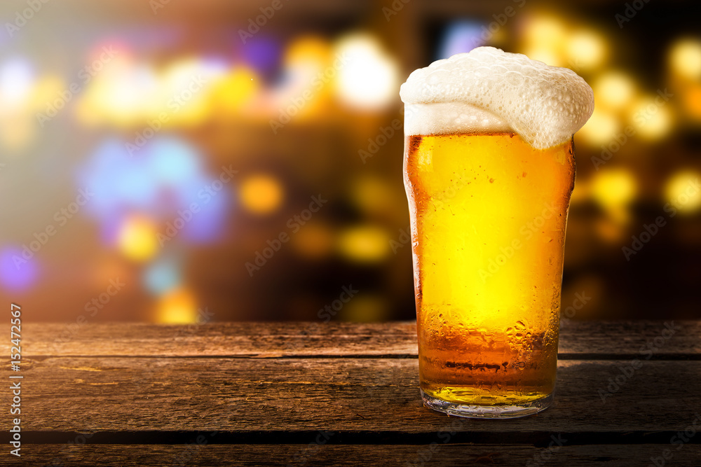 glass of beer on a table in a bar on blurred bokeh background - obrazy, fototapety, plakaty 