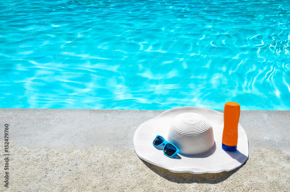 Naklejka premium Summer hat, sunglasses and sunscreen near the pool