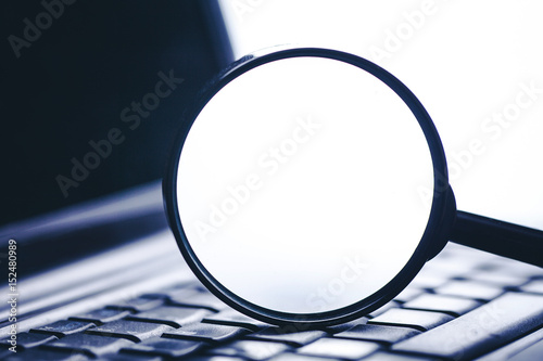 Magnifying glass on laptop keyboard. Internet security background.