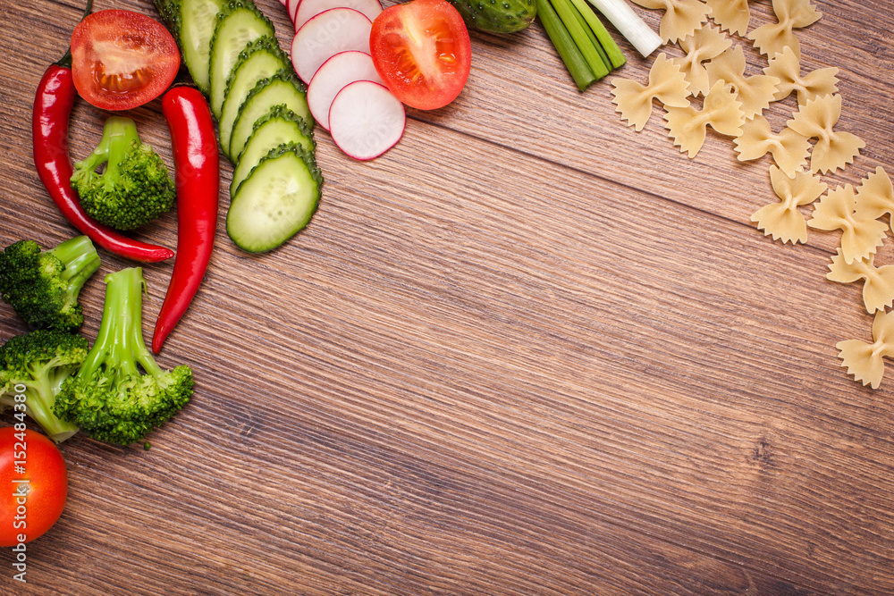 tomato, radish, cucumber, broccoli, onion, chili, pasta, macaroni on a wooden surface. arrangement of sliced vegetables. Top view with copy space for text tomato, radish, cucumber, broccoli, onion, chili, pasta, macaroni on a wooden surface. arrangement of sliced vegetables. Top view with copy space for text
