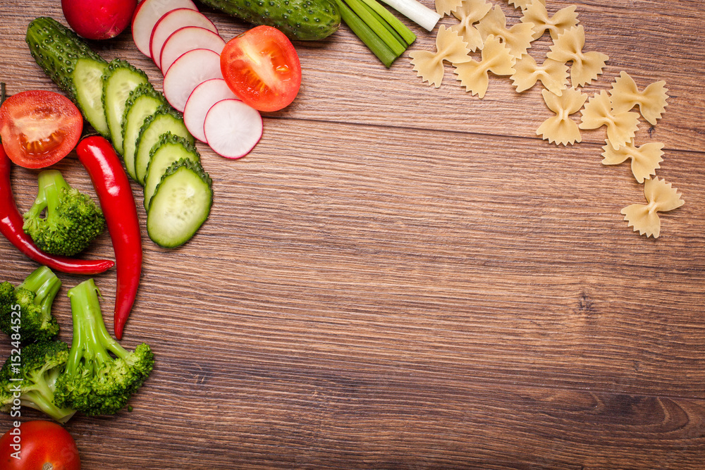 tomato, radish, cucumber, broccoli, onion, chili, pasta, macaroni on a wooden surface. arrangement of sliced vegetables. Top view with copy space for text