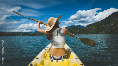 Young woman with long hair and hat kayaking in sun on lake
