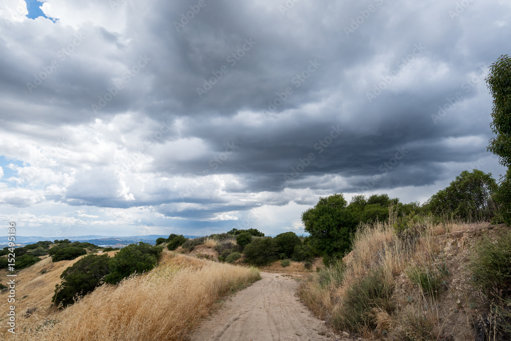 A hiking path heads toward storm clouds in California's San Gabriel mountains.