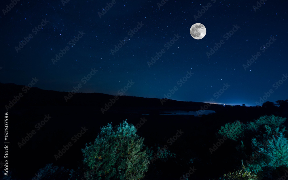Mountain Road through the forest on a full moon night. Scenic night landscape of dark blue sky with moon. Azerbaijan. Long shutter photo