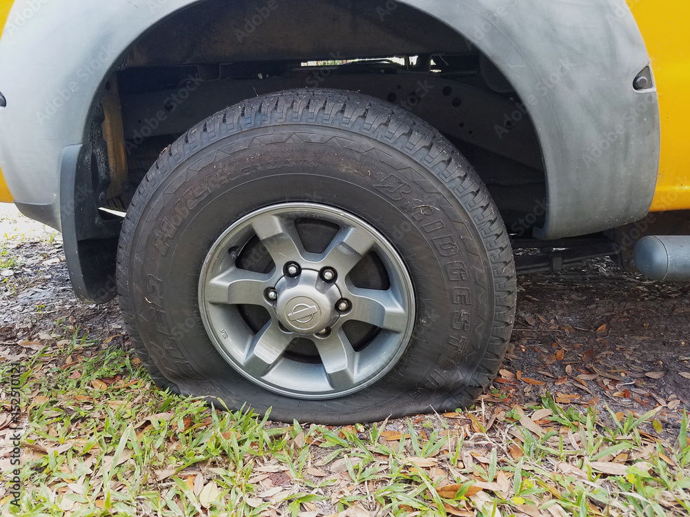 Flat back tire on yellow truck had a cut tread parked on grass.