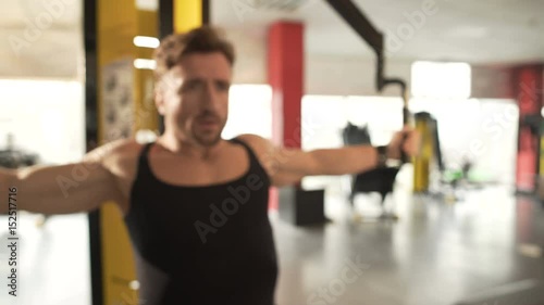 Middle-aged fit male doing pectoral fly workout in gym, training his arm muscles