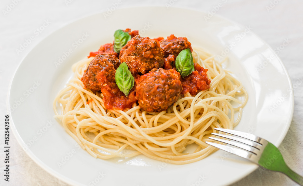 Spaghetti pasta with meatballs in tomato sauce and basil leaves against white background
