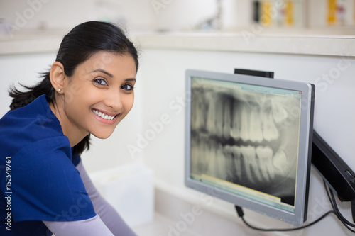 Closeup portrait of allied health dental professional in blue scrubs examining dental x-ray on computer screen, isolated dentist office