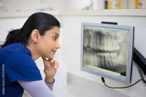 Closeup portrait of allied health dental professional in blue scrubs examining dental x-ray on computer screen, isolated dentist office