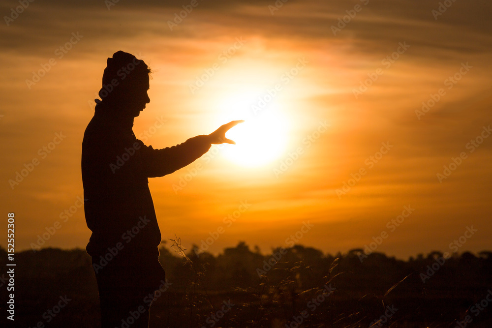 Silhouette of a man standing and rise his hands up in the air during sunset