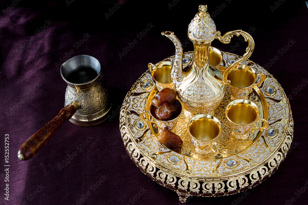 Fototapeta premium Still-life with traditional golden Arabic coffee set with dallah, coffee pot and dates. Dark background. Horizontal photo
