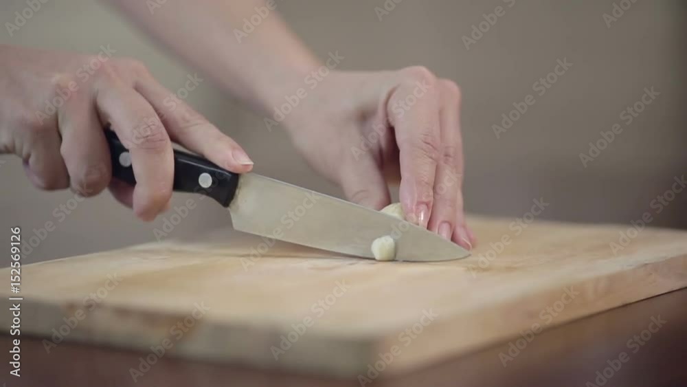 00:00 | 00:00 1×  Close-up of professional cook chopping garlic on cutting board, young woman preparing meal at the kitchen table.