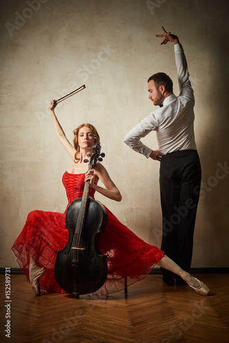 Female ballet dancer in red dress and pointe playing on antique black cello and male dancing latin