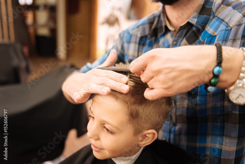 Cute delighted boy having the ends of his hair cut