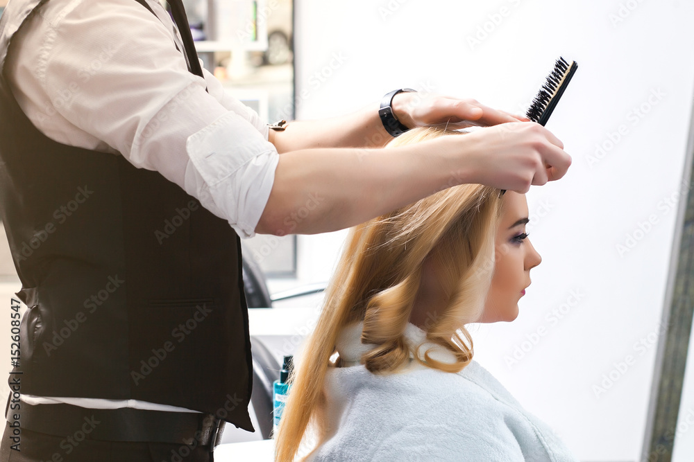 handsome Hairdresser does a hairstyle for a blonde girl in a beauty salon