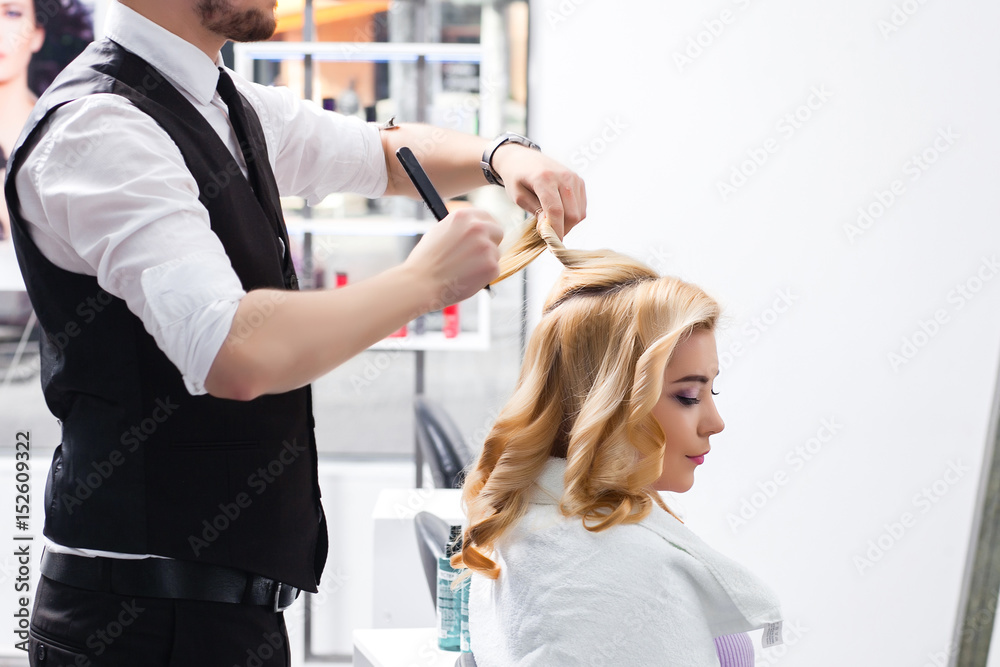 Obraz premium handsome Hairdresser does a hairstyle for a blonde girl in a beauty salon