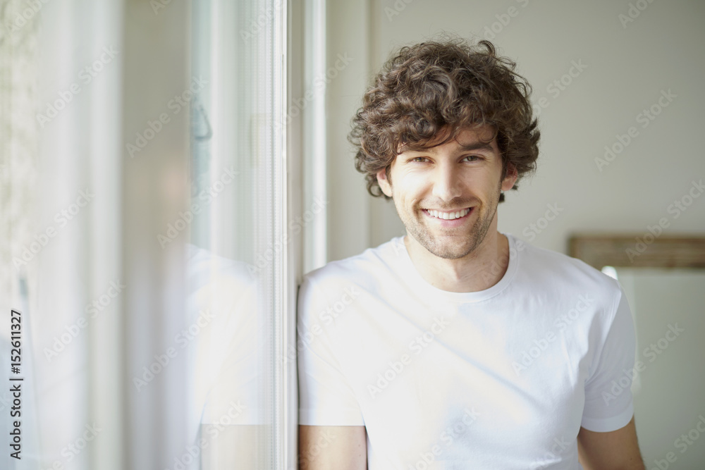 Confident young man portrait. Shot of happy young man standing in living room at the window. Confident young man portrait. Shot of happy young man standing in living room at the window.