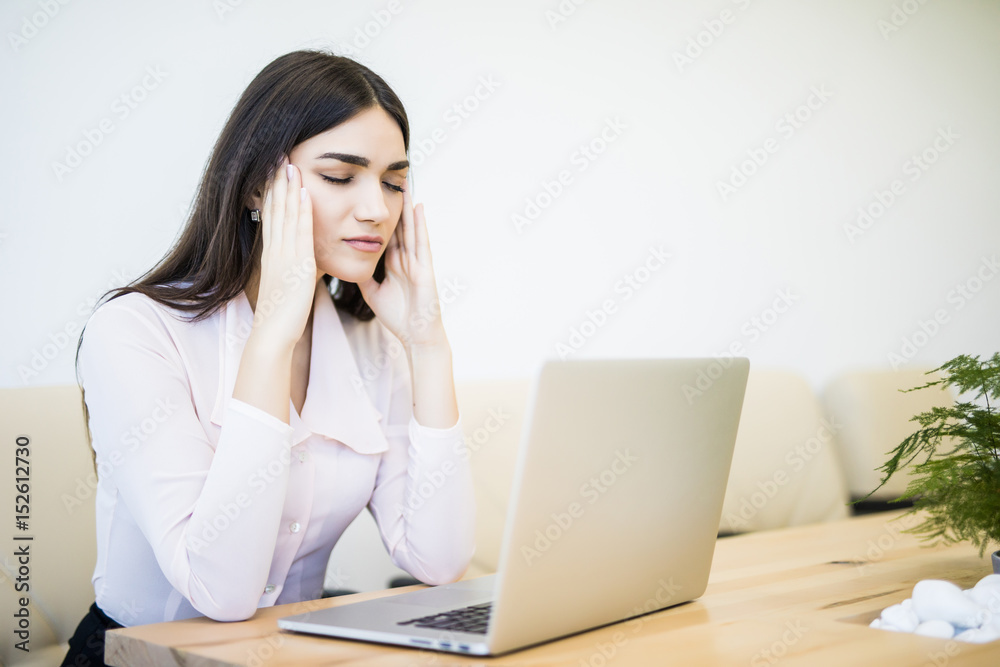 Young attractive woman at modern office desk, working on laptop, massaging temples to forget about constant headaches, noisy loud office giving a migraine. Young attractive woman at modern office desk, working on laptop, massaging temples to forget about constant headaches, noisy loud office giving a migraine.