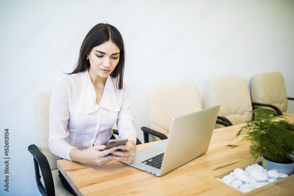 Beautiful young business woman is using a smartphone and smiling while working in modern office Beautiful young business woman is using a smartphone and smiling while working in modern office