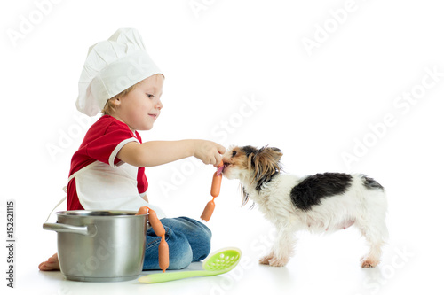 Role-playing game. Kid boy plays chef with pet. Child weared cook feeds dog. photo