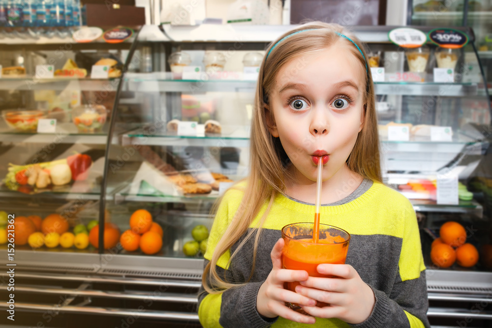 A girl stands near a showcase and drinks juice Through the straw in a cafe A girl stands near a showcase and drinks juice Through the straw in a cafe