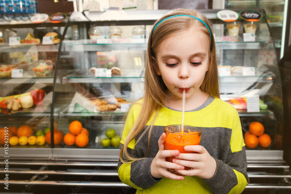 A girl stands near a showcase and drinks juice Through the straw in a cafe A girl stands near a showcase and drinks juice Through the straw in a cafe