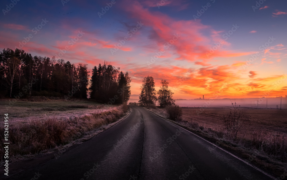 Scenic landscape with road and colorful sunrise at  foggy autumn morning in Finland.