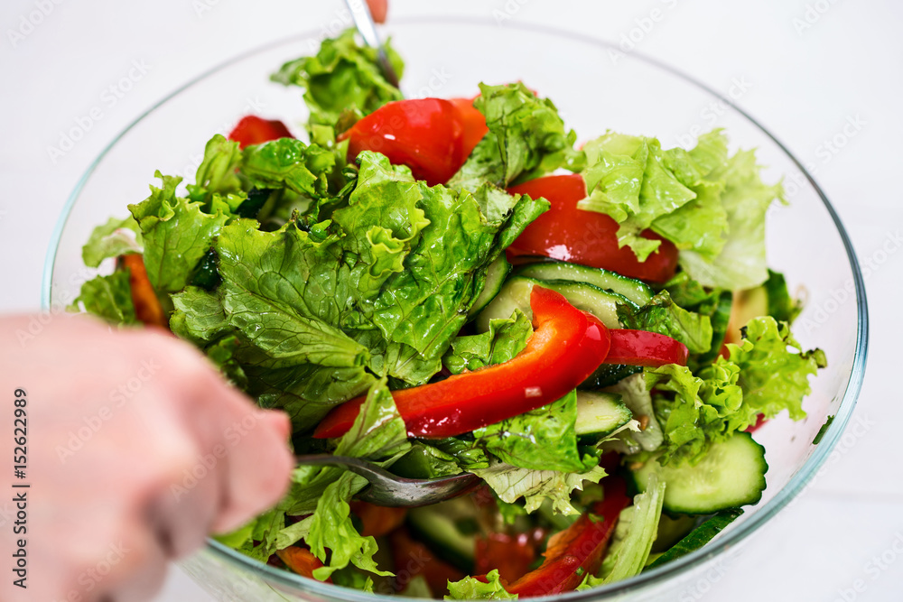 Young woman dressing vegetable salad with olive oil on a white background Young woman dressing vegetable salad with olive oil on a white background