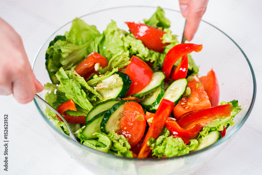 Young woman dressing vegetable salad with olive oil on a white background Young woman dressing vegetable salad with olive oil on a white background