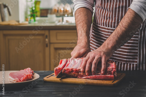 Man cuts of fresh piece of meat on a wooden cutting board in the home kitchen