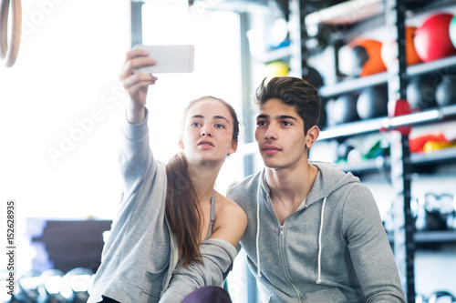 Fit couple in modern crossfit gym with smartphone.