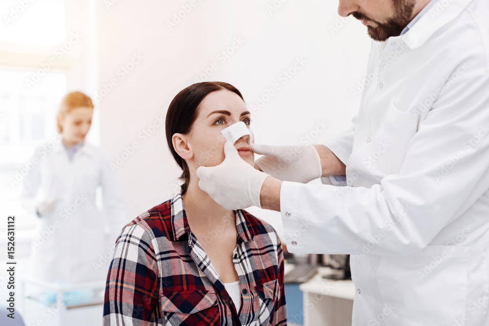 Obraz premium Nice serious woman having a medical dressing on her nose