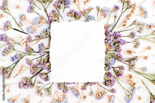 Empty white paper blank on blue and purple dried flowers frame on white background. Flat lay, top view
