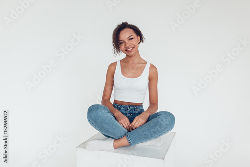 Beautiful african girl in white tops sitting on white background.