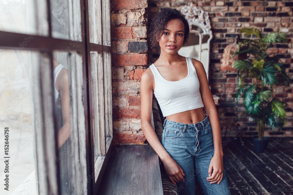 Naklejka premium Beautiful african girl in white top standing near the window.